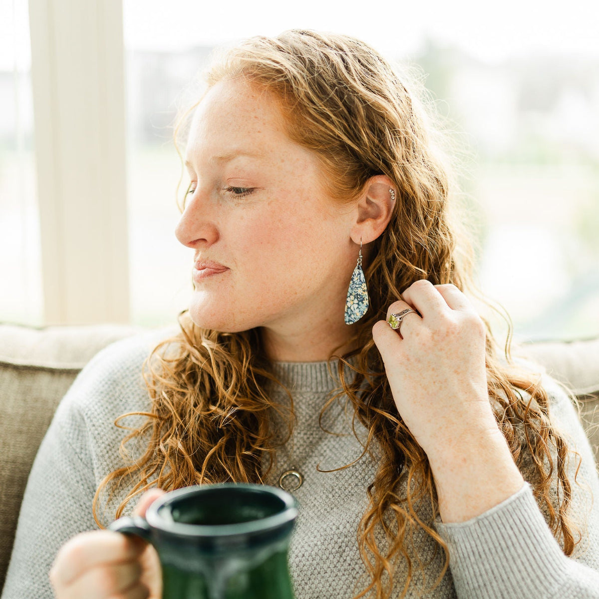 Woman holding a cup of coffee while showcasing the Eliza blue floral cork teardrop earrings 