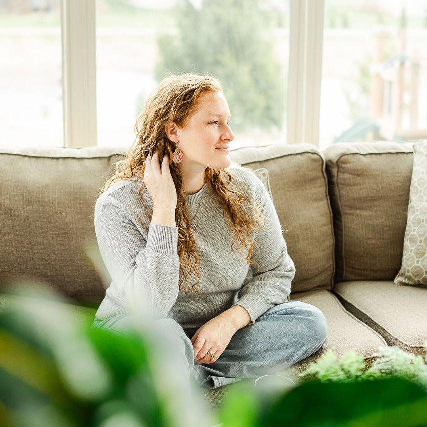 Woman wearing the Cora Summer Garden cork and walnut earrings on a couch