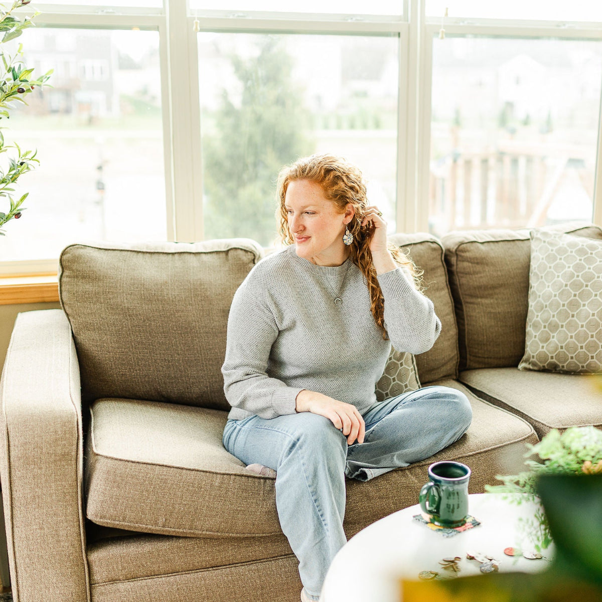 Woman showcasing the Cora heirloom floral cork and walnut earrings on a couch