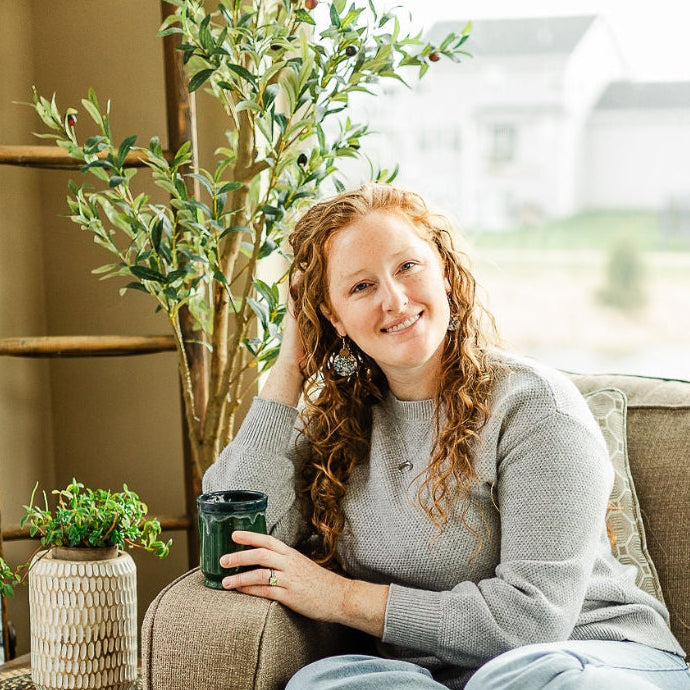 Woman on a couch wearing the Cora Blue Floral cork and walnut earrings