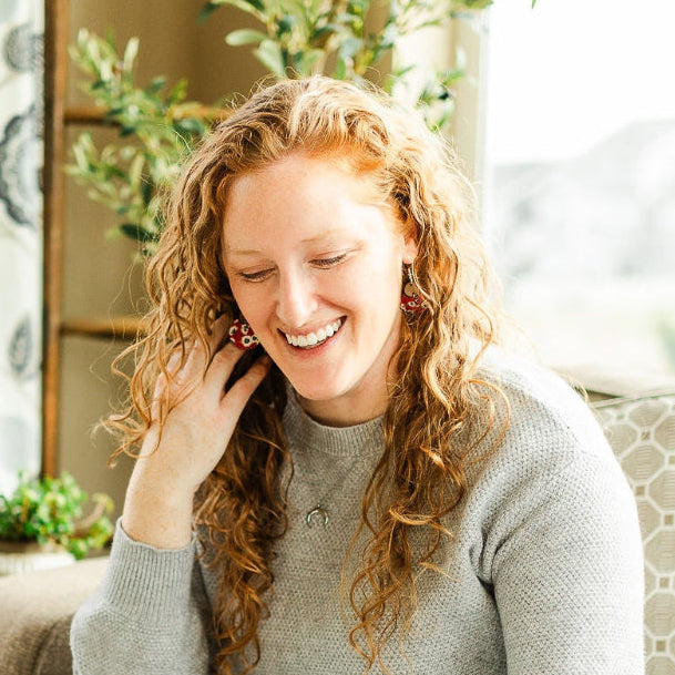 Woman wearing the Fireworks pattern cork and walnut earrings while sitting on a couch