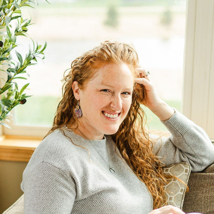 Woman sitting on a chair while showcasing the Cora Star Spangled cork and walnut earrings 