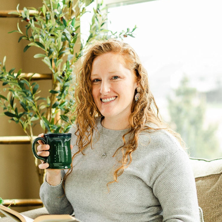 woman holding a cup and a book on a sofa 