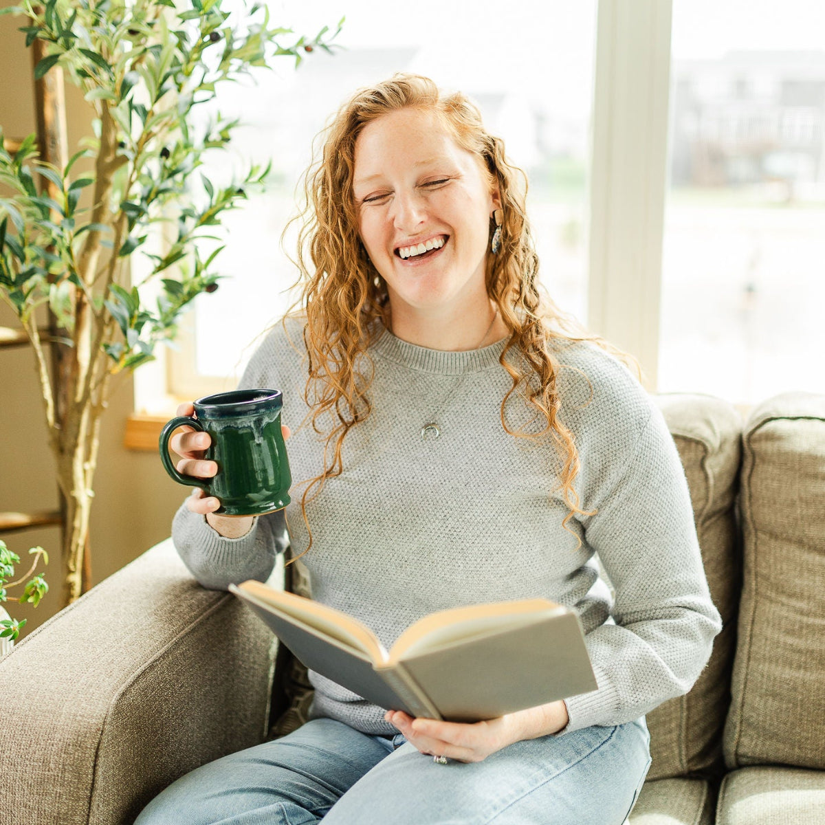 Woman laughing while holding a cup and a book