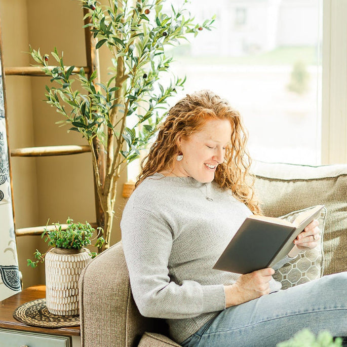 woman reading a book on a sofa while wearing the Deep red wine earrings with silver starburst detail and rich tone