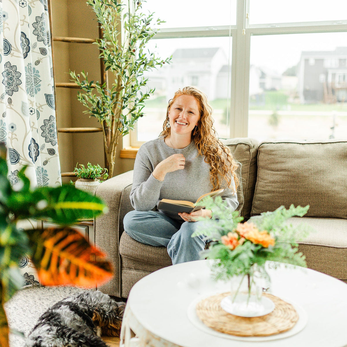 Woman sitting on a couch while holding a book and smiling
