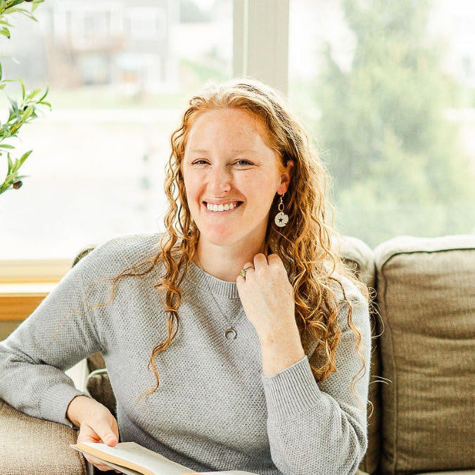 Woman on a couch holding a book and wearing a Pair of Elizabeth blue stars cork hexagon earrings