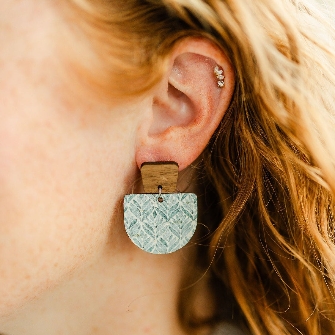 Close-up of a person wearing textured earrings with a blurred background