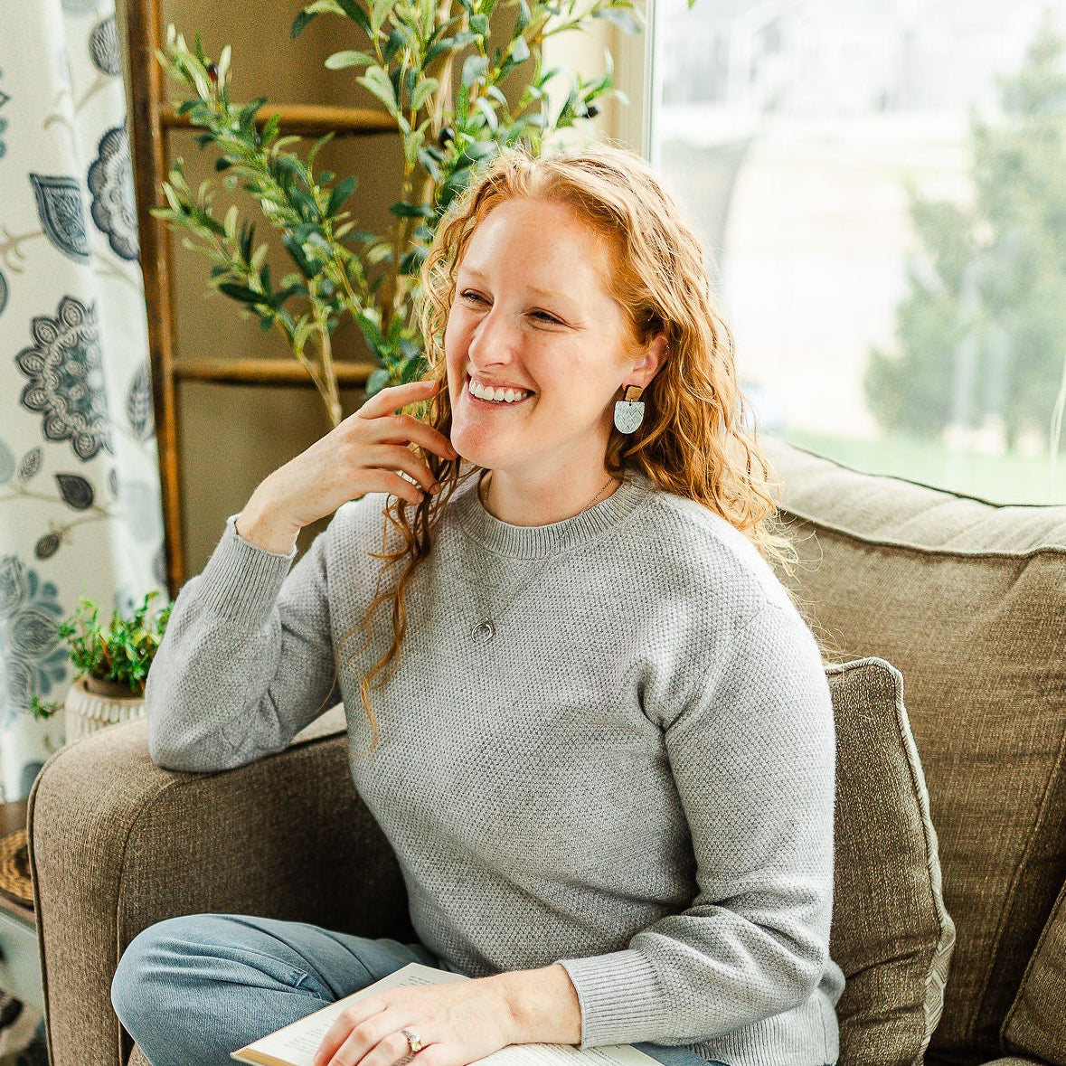 Woman sitting on a couch with a book, smiling in a cozy living room.