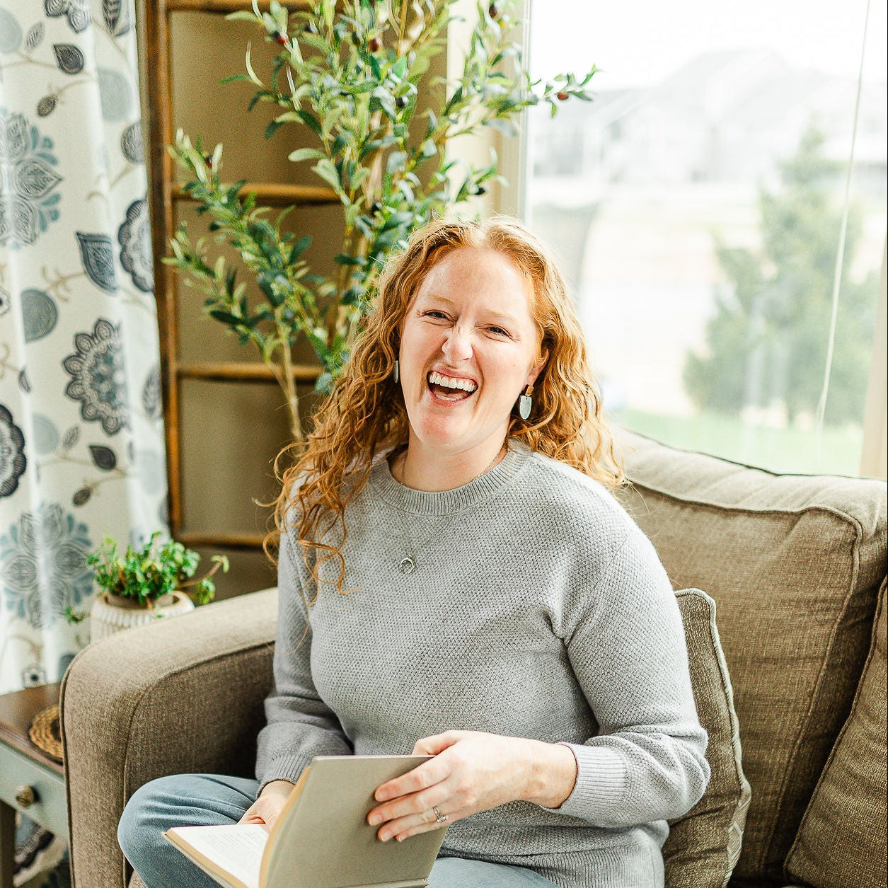 Woman sitting on a couch holding a book in a cozy living room.