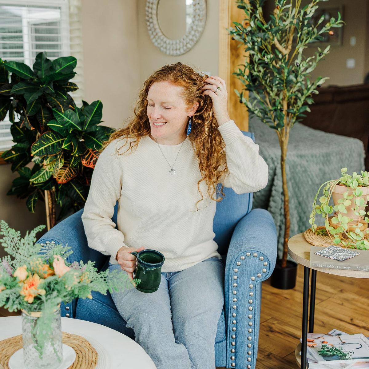Woman sitting on a couch while holding a mug and showcasing the Creek+Elm earring
