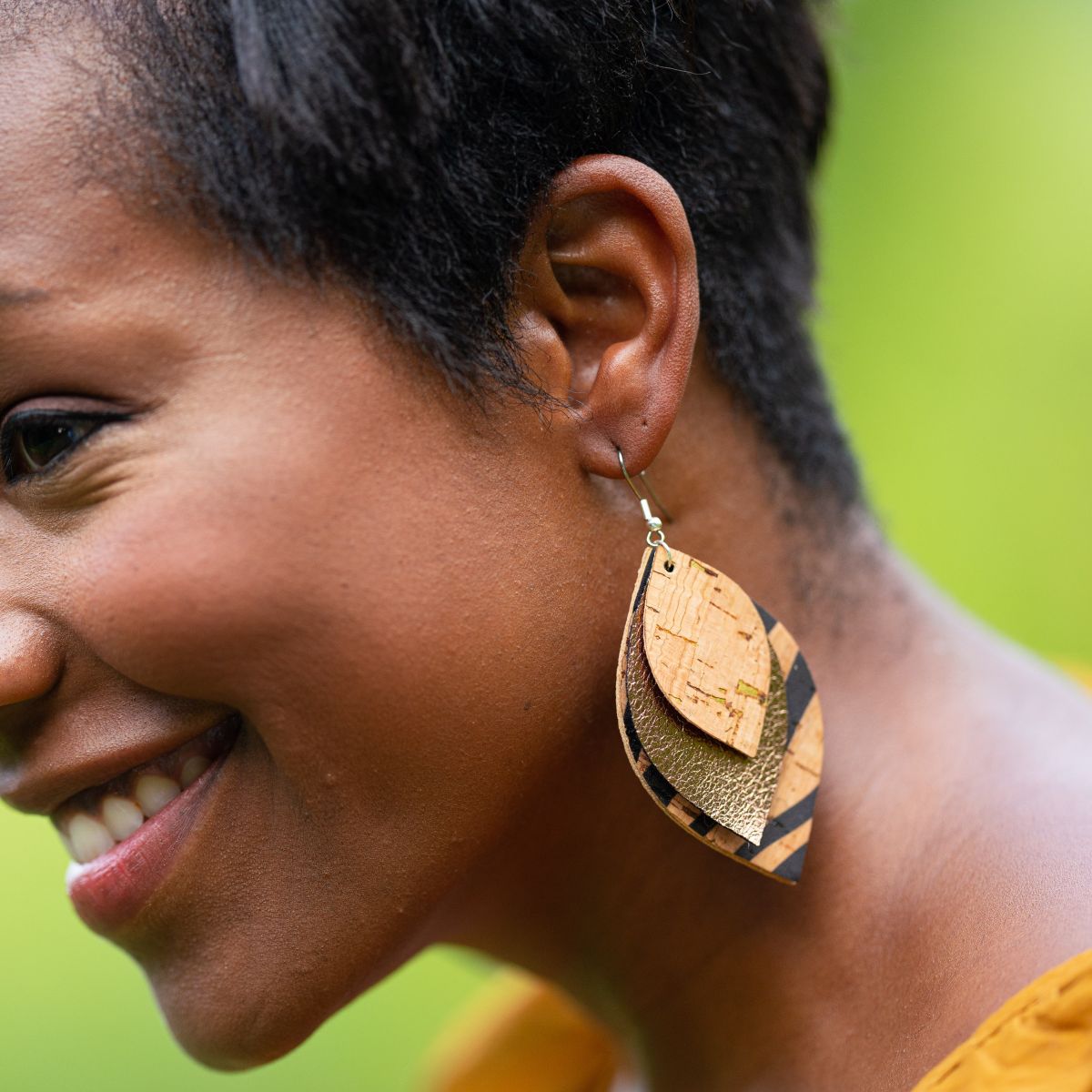 Close-up of a woman wearing a gold and black leaf-shaped earring with a blurred green background