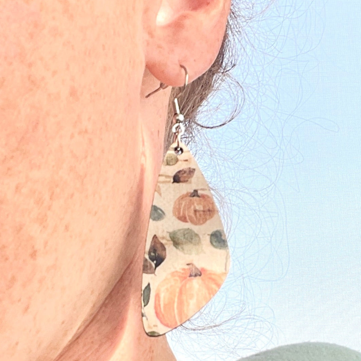Close-up of a person wearing pumpkin print earrings with a window in the background.