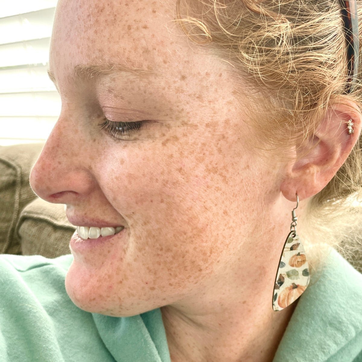 Close up of a woman wearing teardrop shaped cork earrings with a fall pumpkin pattern