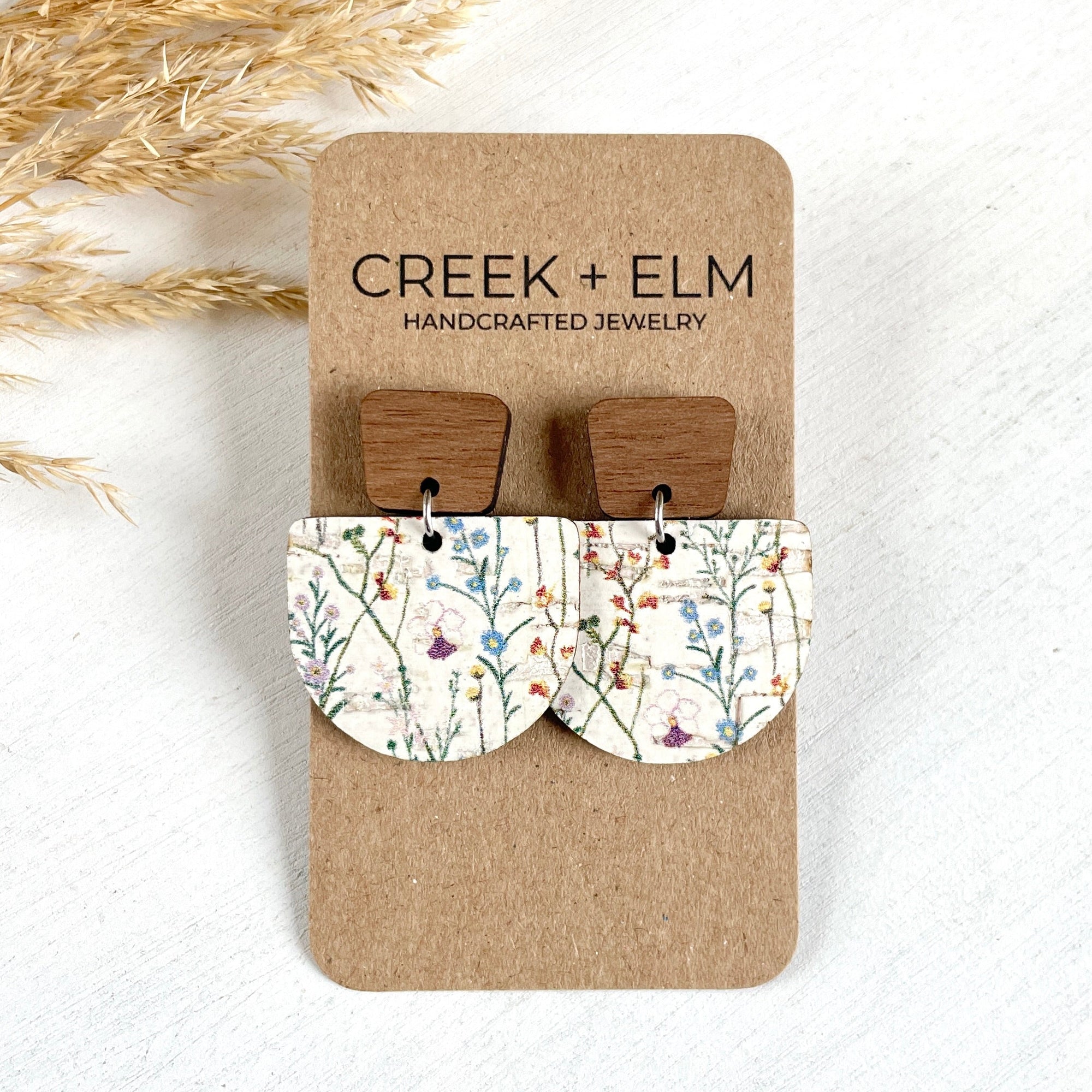 Pair of wildflower cork earrings on a Creek + Elm branded card with dried plants in the background