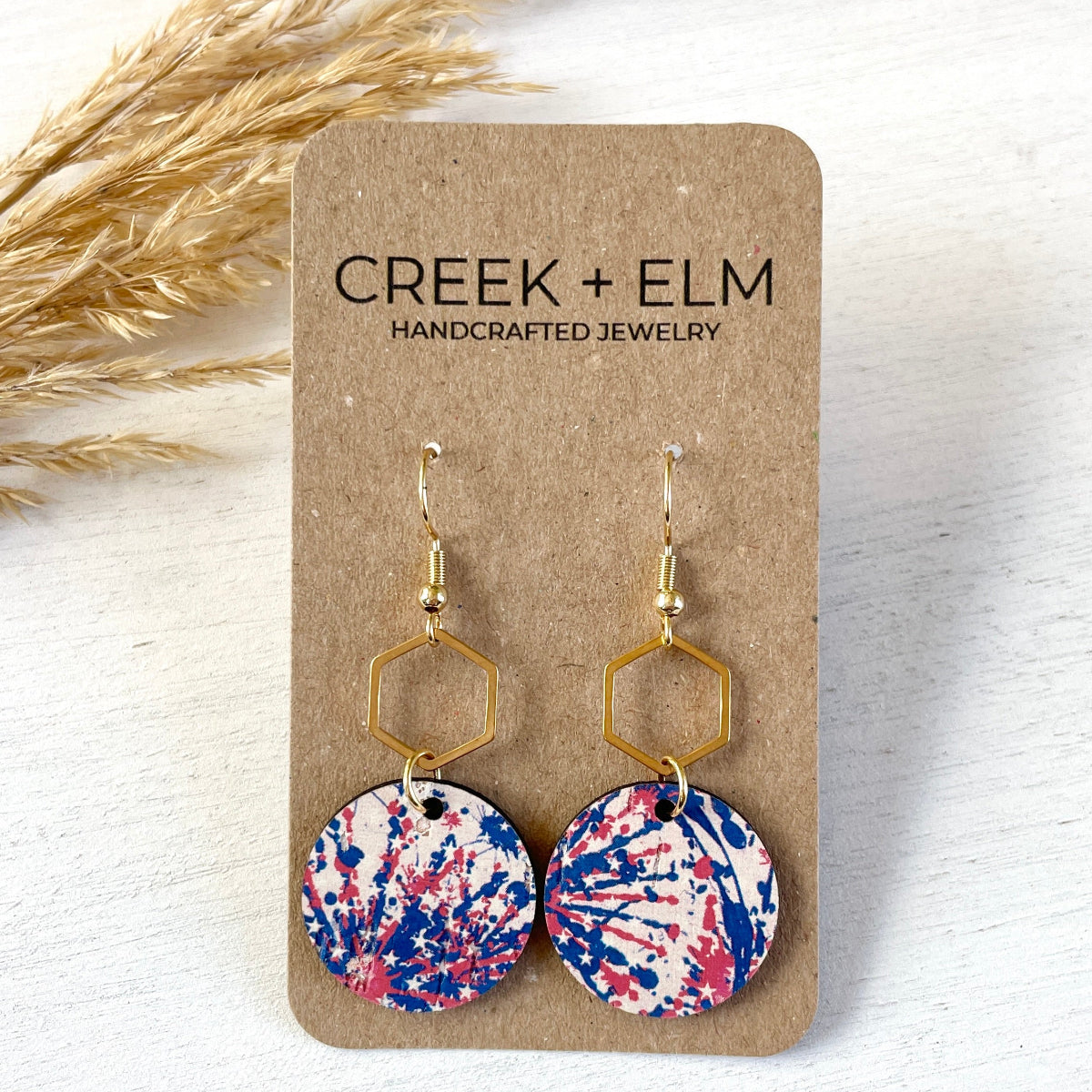 Gold Elizabeth star spangled cork and hexagon earrings on plain background