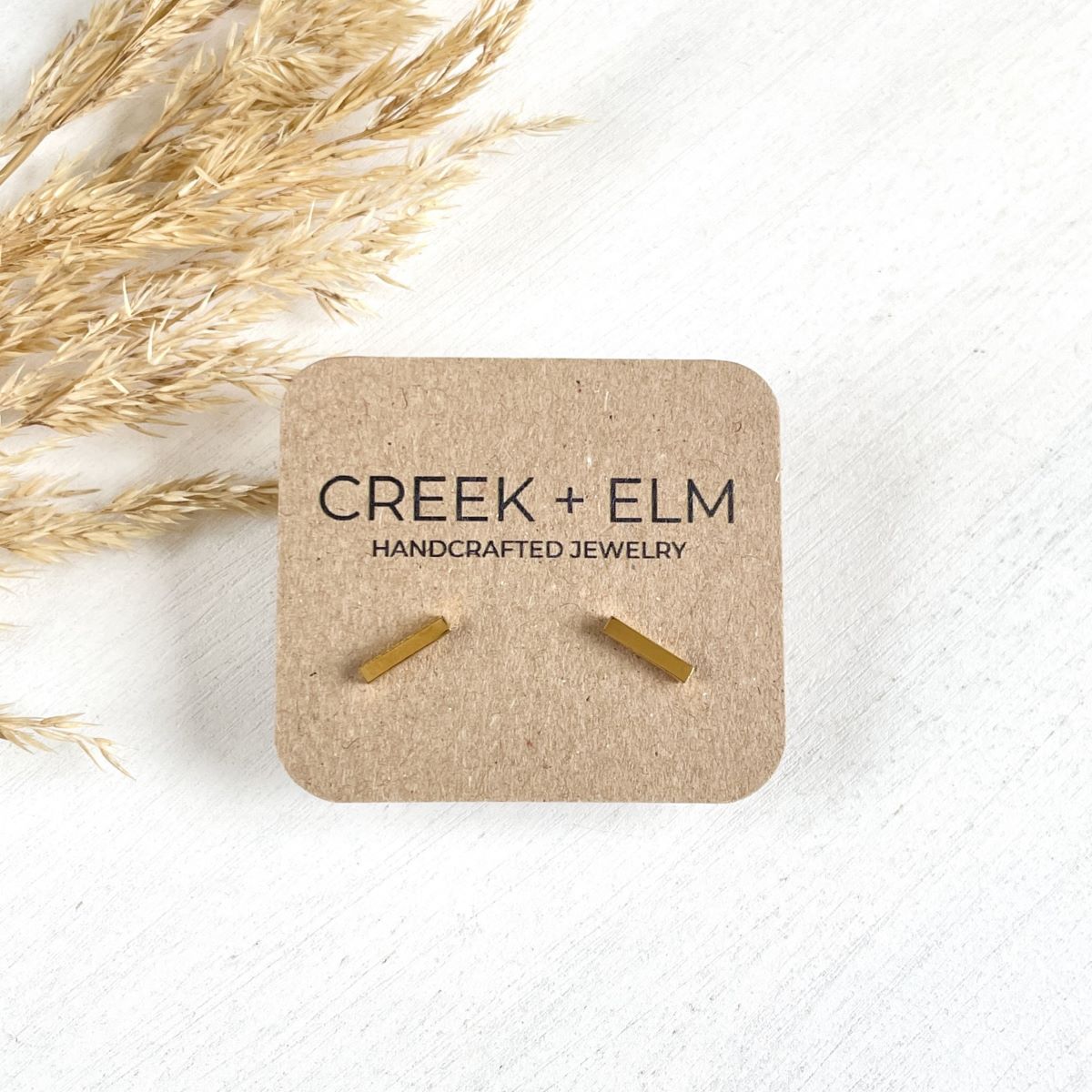 Gold stainless steel bar stud earrings on Creek + Elm packaging