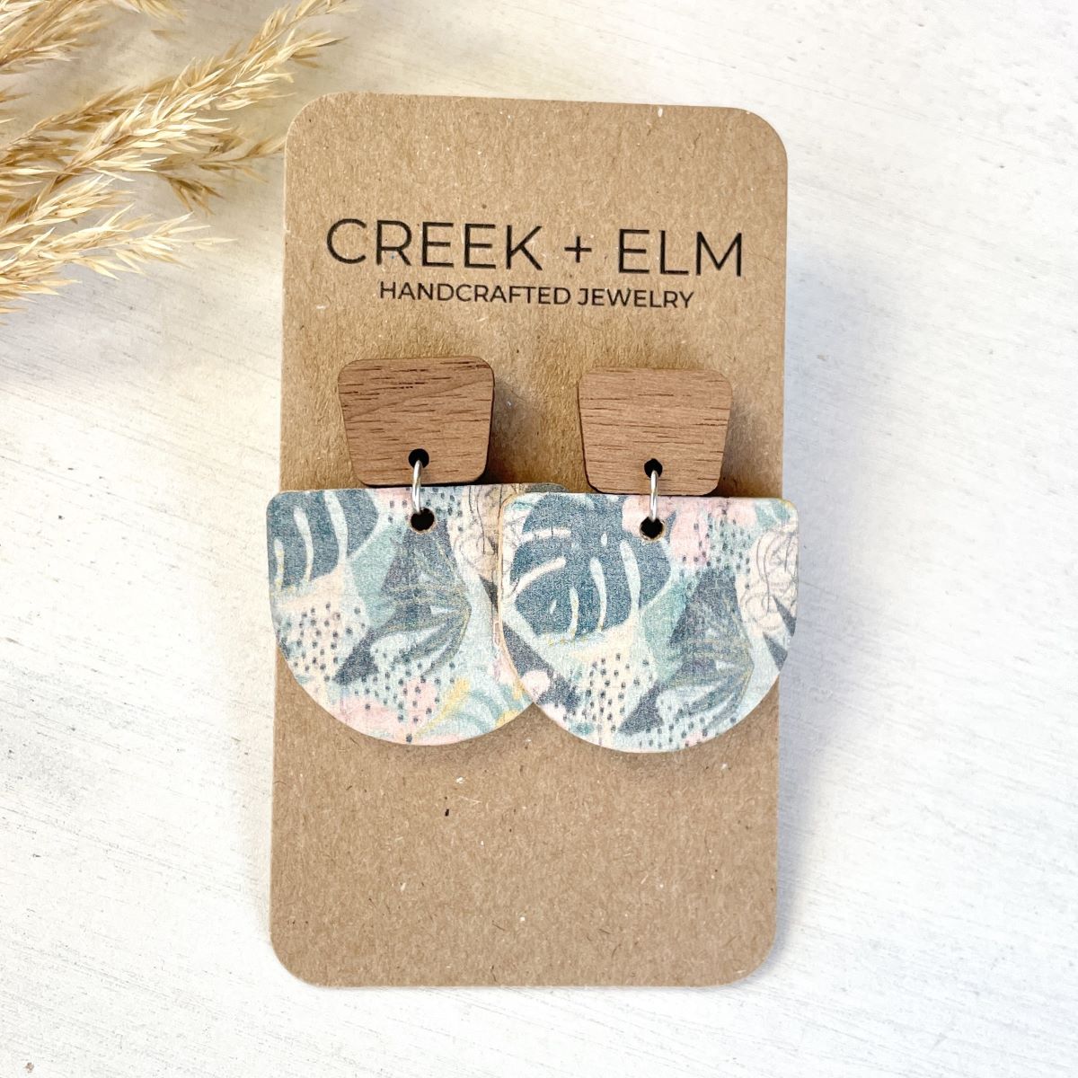 Monstera leaf cork earrings with walnut geometric post and half-circle design on a packaging