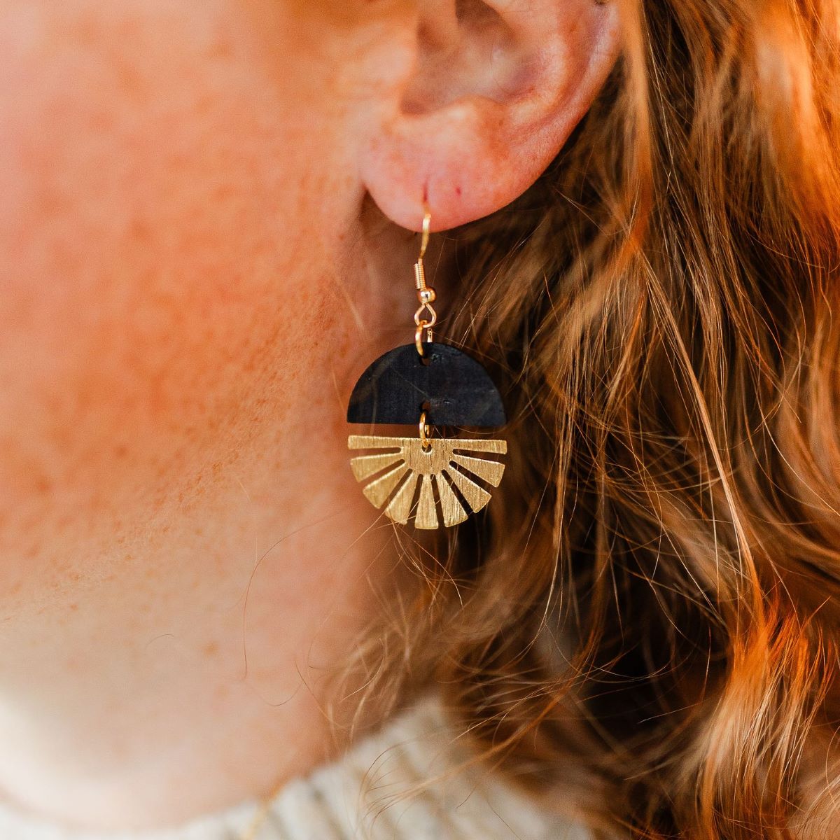 Black earrings with gold starburst detail and sleek finish on packaging
