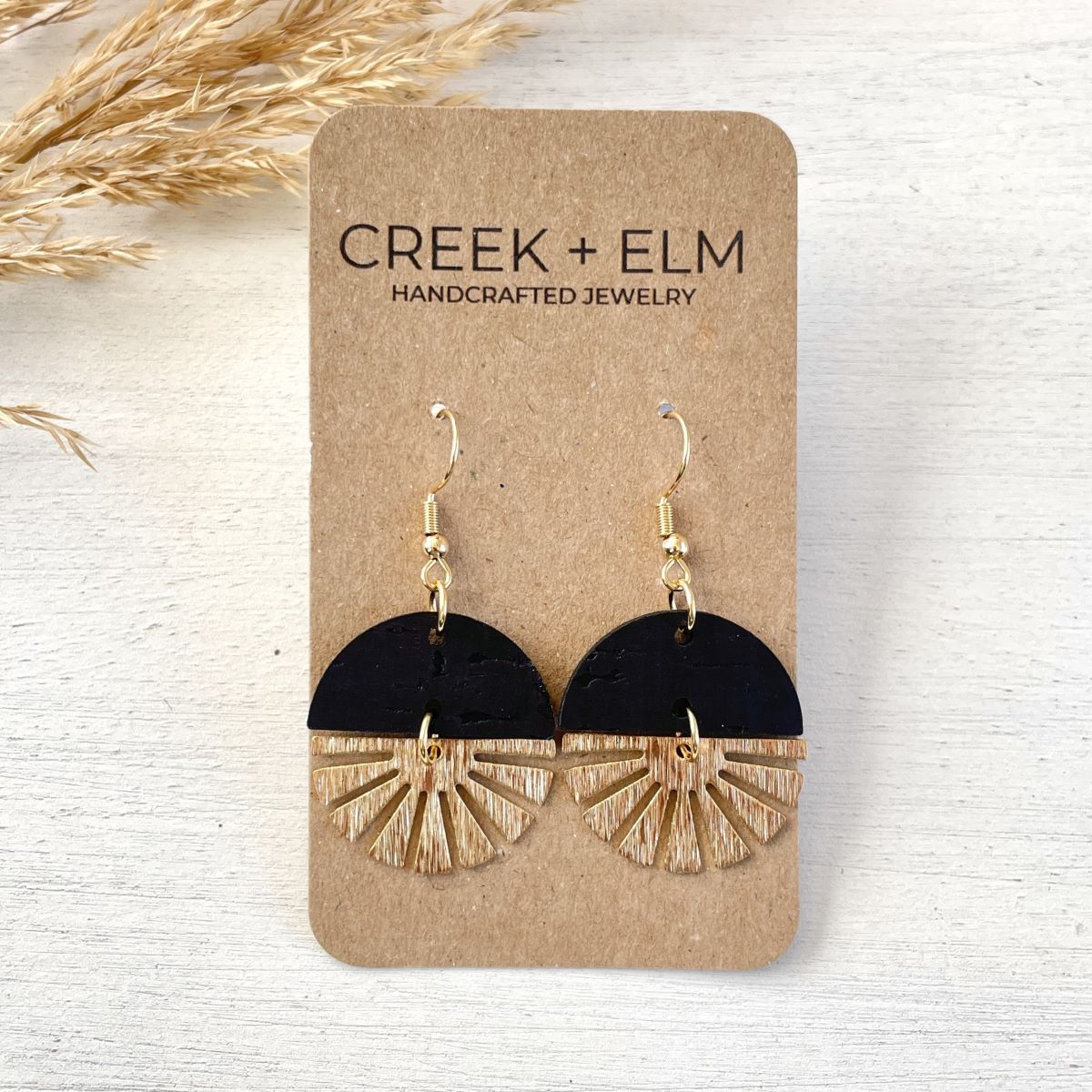 Black earrings with gold starburst detail and sleek finish on packaging