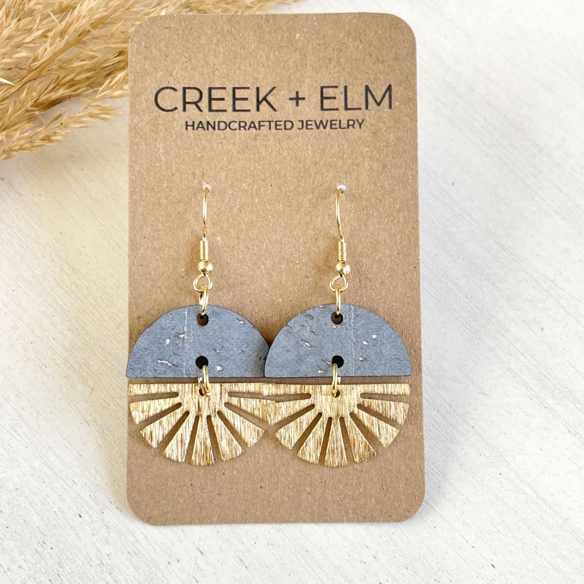 Pearl gray earrings with gold starburst detail and neutral tone on packaging 