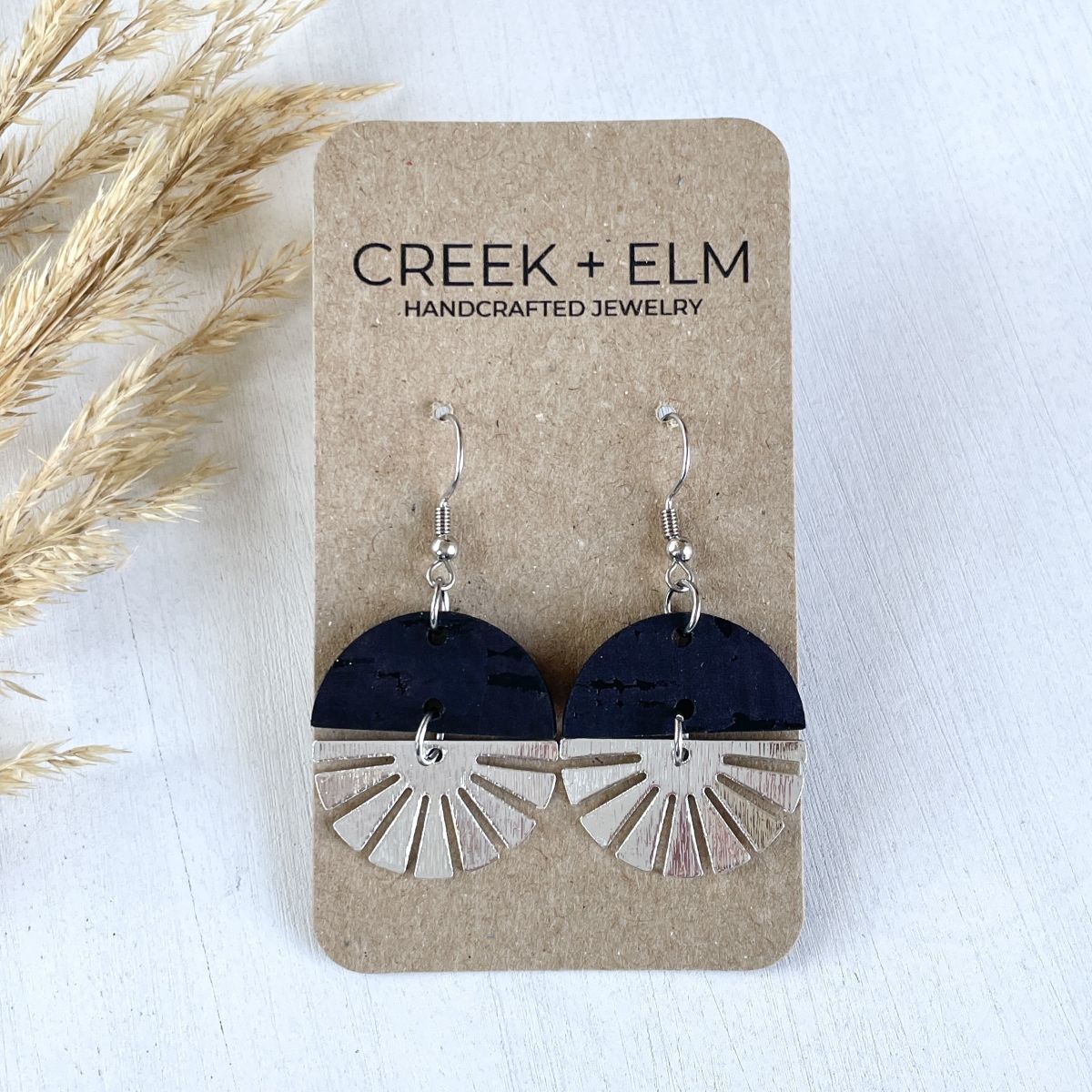 Black earrings with silver starburst detail and clean modern finish on packaging