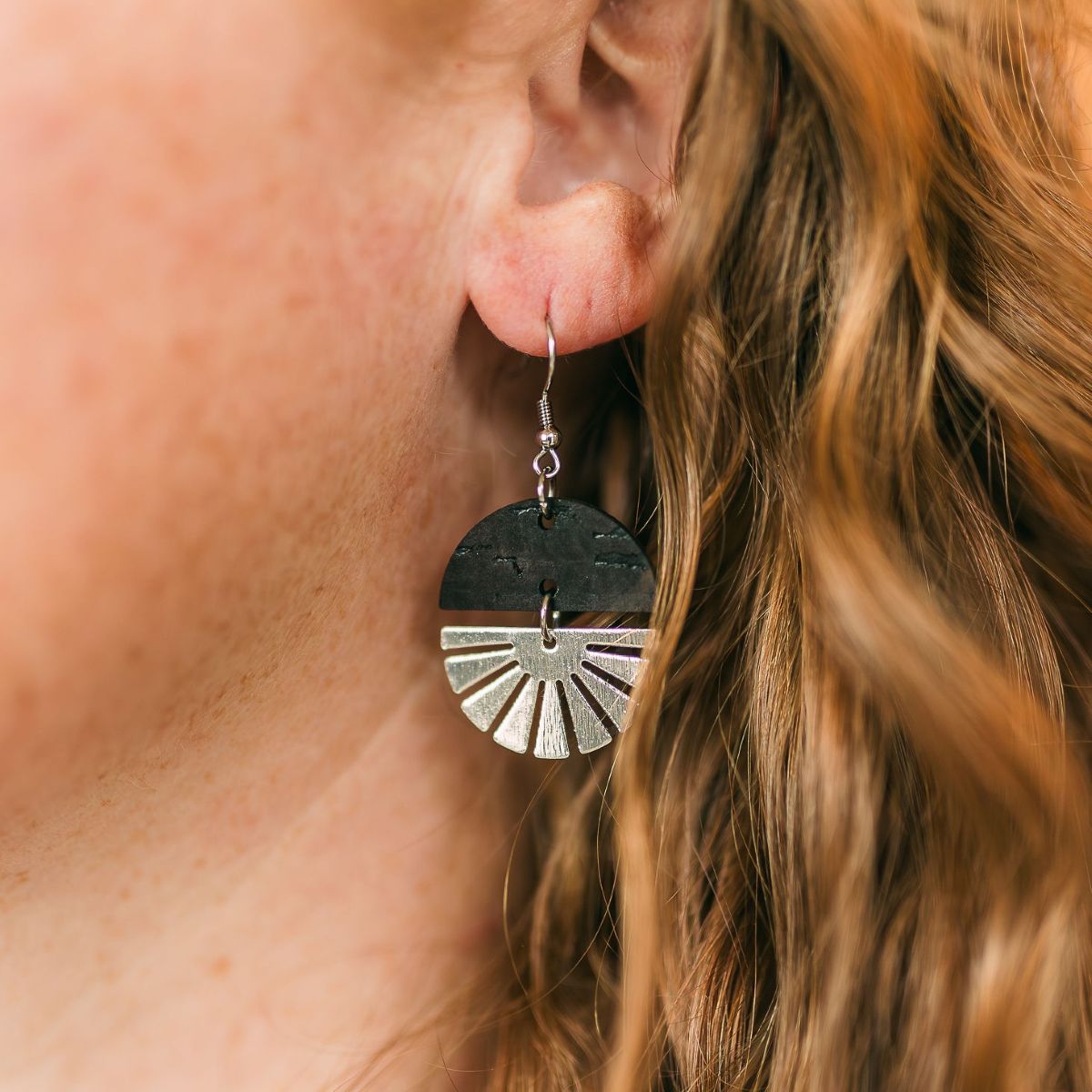 Black earrings with silver starburst detail and clean modern finish on packaging
