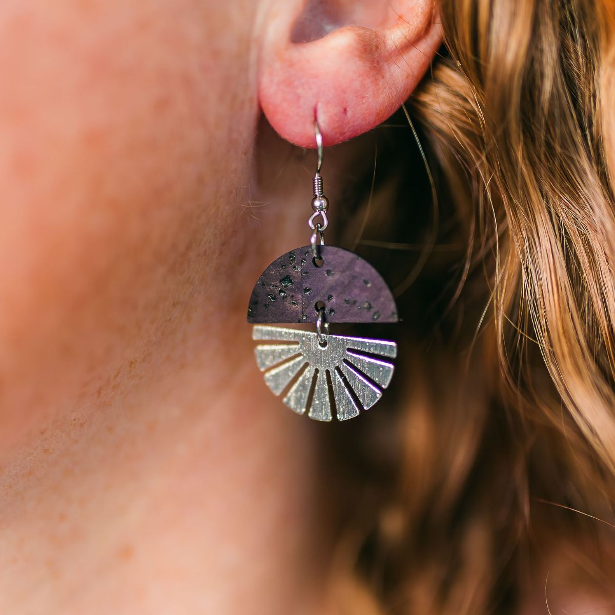 Eggplant-toned earrings with silver starburst accent and soft finish on packaging 