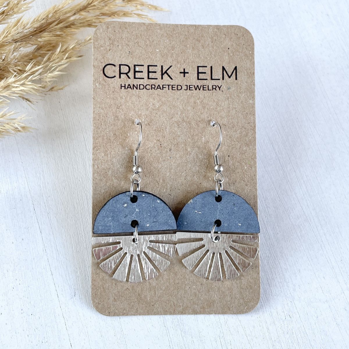Pearl gray earrings with silver starburst detail in a soft neutral tone on packaging