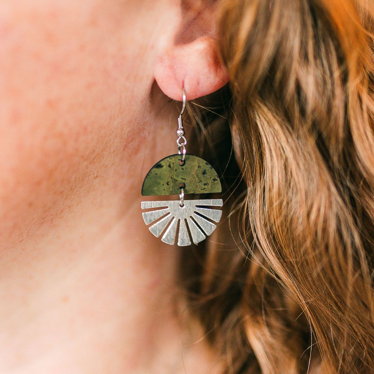 Olive-toned earrings with silver starburst detail and soft natural finish on a packaging