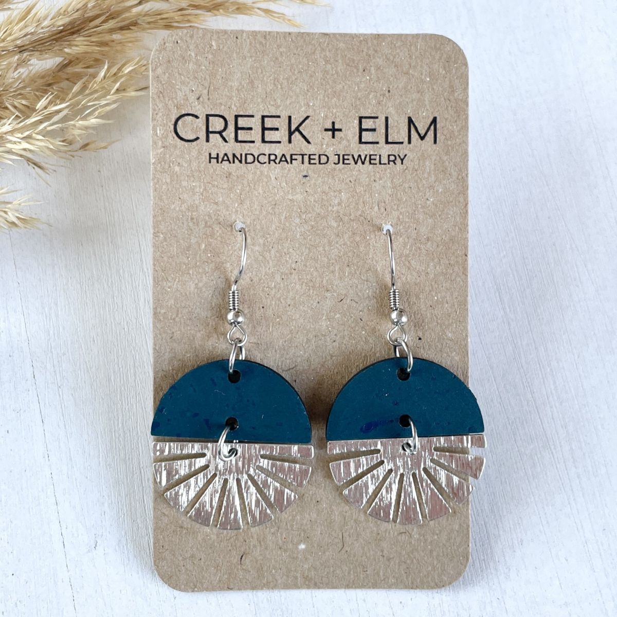 Teal earrings with silver starburst detail and smooth finish on packaging