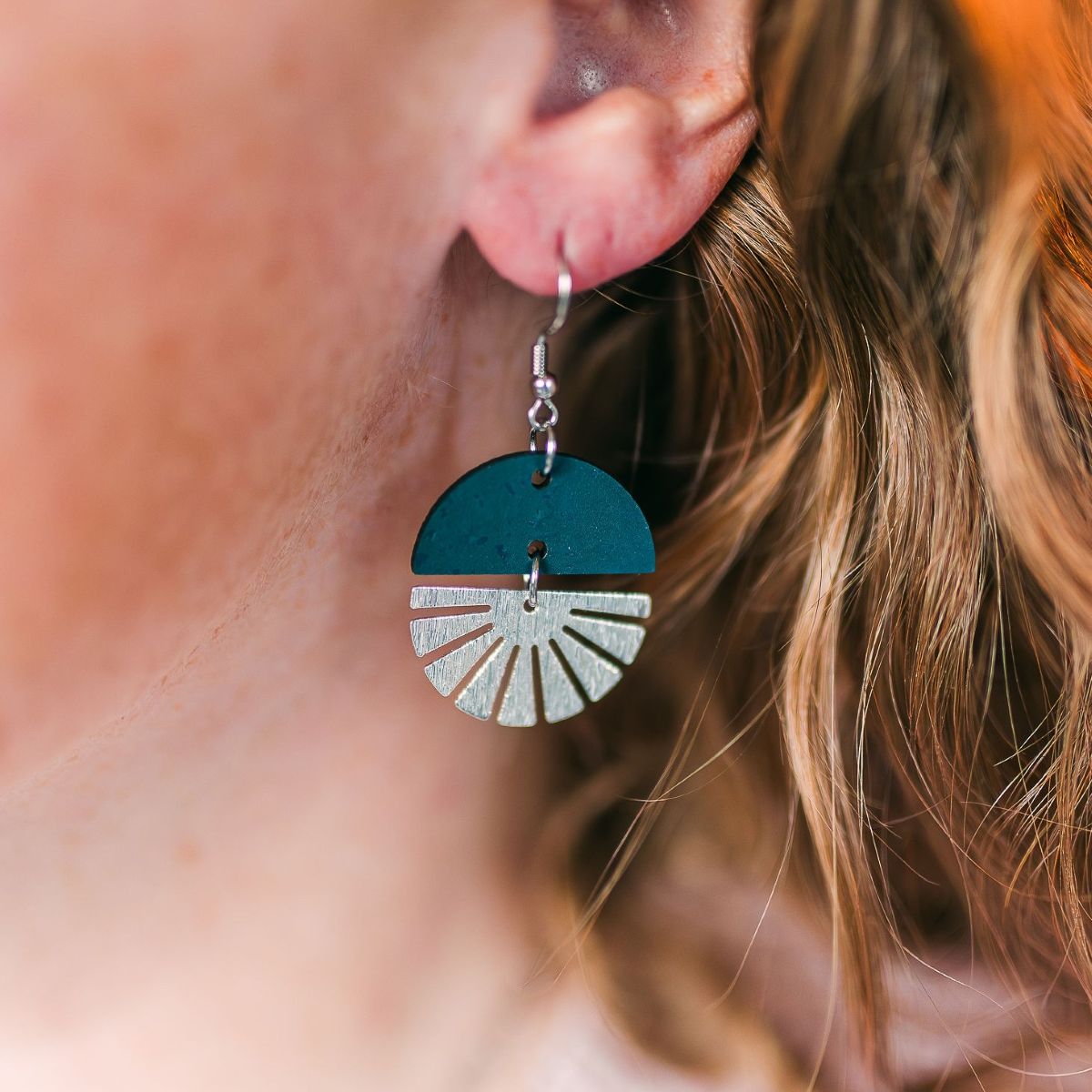 Teal earrings with silver starburst detail and smooth finish on packaging