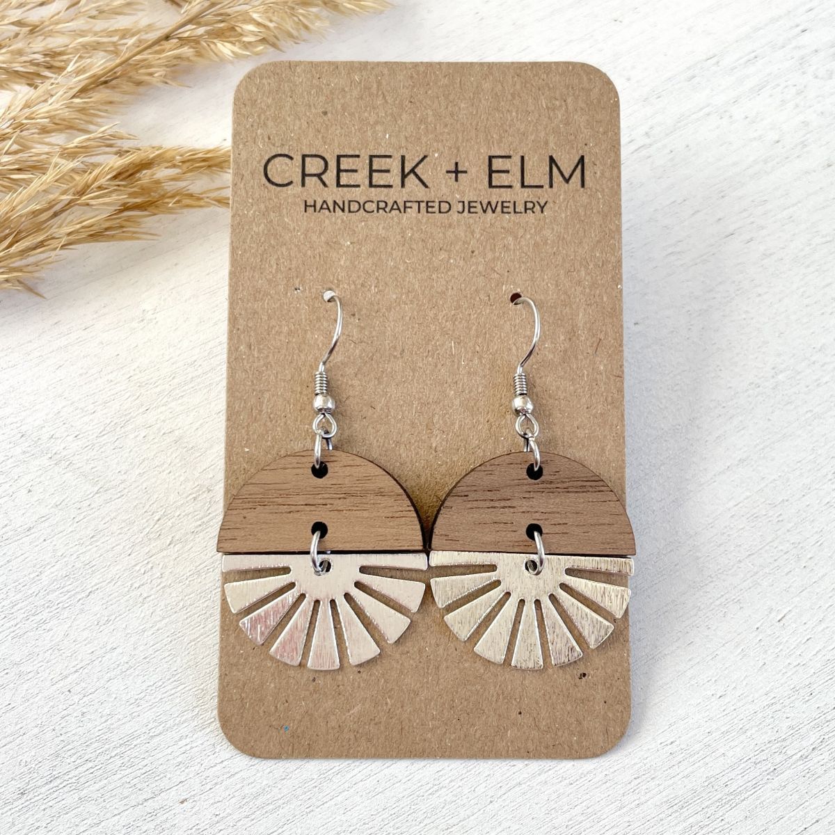 Walnut wood earrings with silver starburst accent and natural grain detail on a packaging