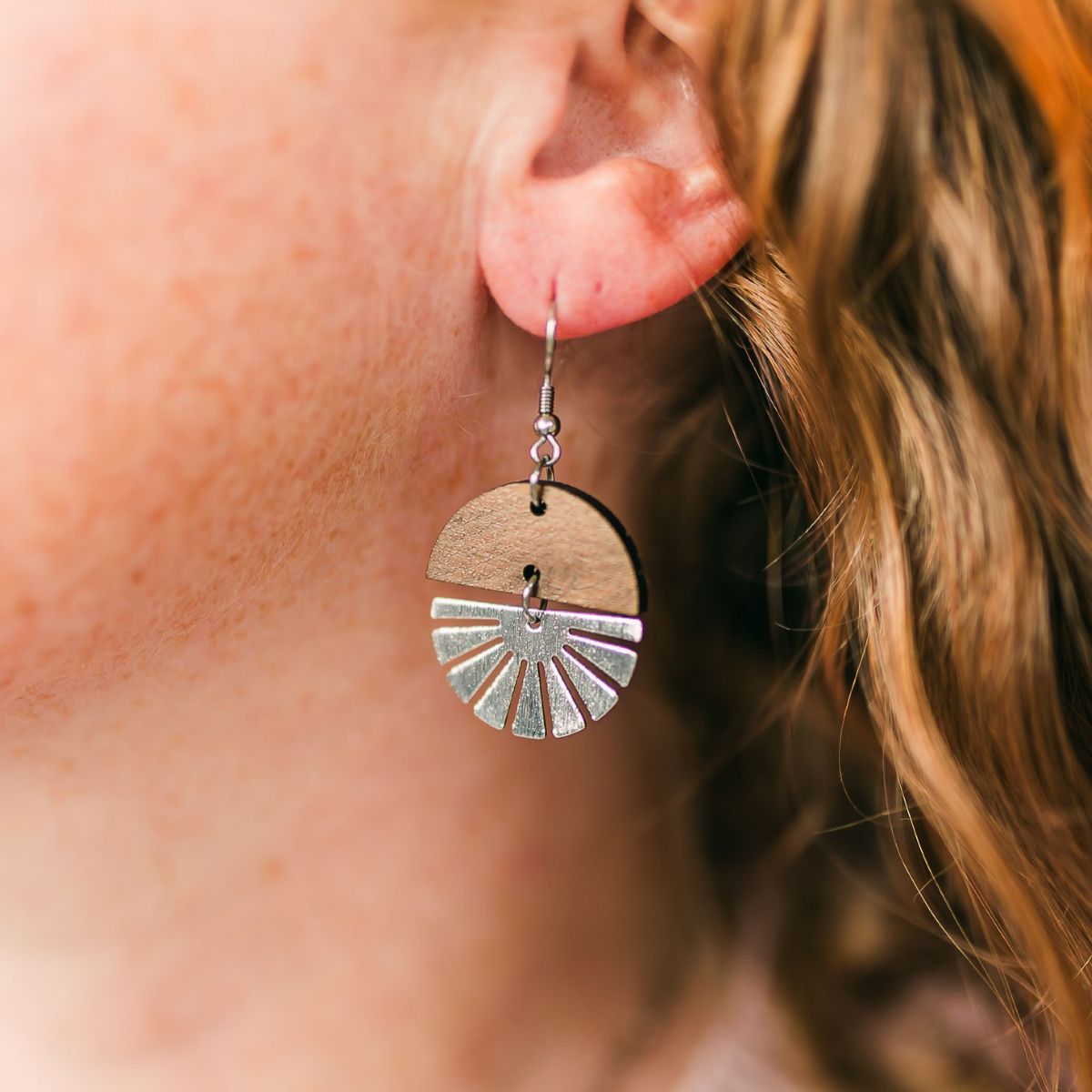 Walnut wood earrings with silver starburst accent and natural grain detail on a packaging