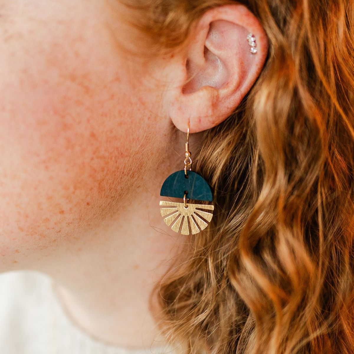 Teal earrings with gold starburst detail and smooth finish on packaging