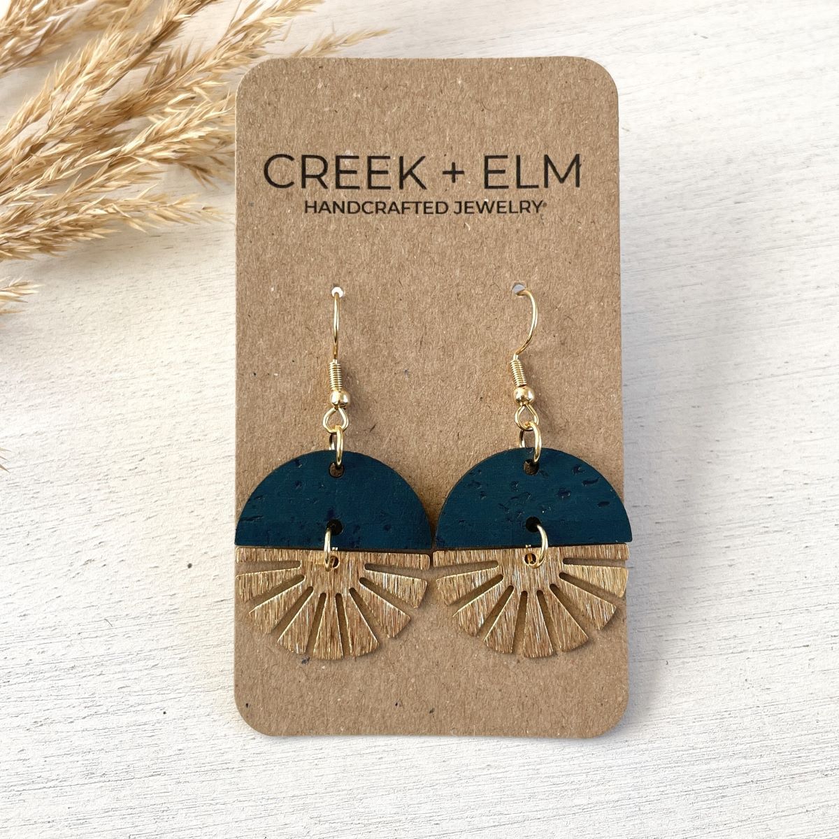 Teal earrings with gold starburst detail and smooth finish on packaging