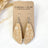 A pair of teardrop-shaped dangle earrings with a white botanical pattern on a tan background, displayed on a brown kraft card labeled 'CREEK + ELM HANDCRAFTED JEWELRY'.