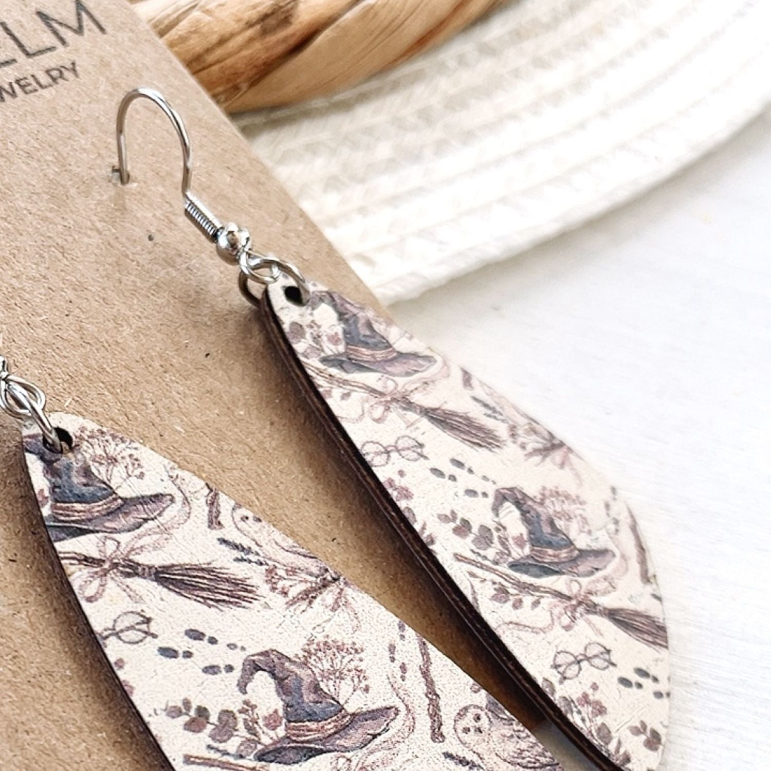 A pair of long teardrop-shaped dangle earrings with a vintage witch illustration pattern, displayed on a brown kraft card.