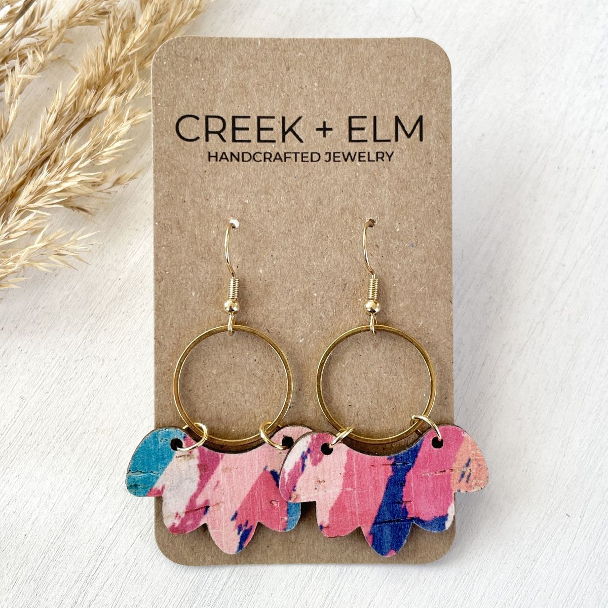 Pair of hoop earrings with colorful elephant charms on a Creek + Elm branded card.
