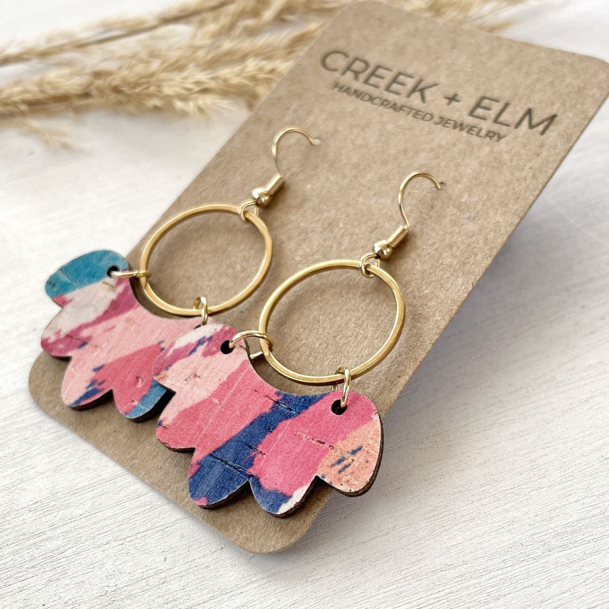 Pair of gold hoop earrings with colorful leaf-like charms on a Creek &amp; Elm branded card.