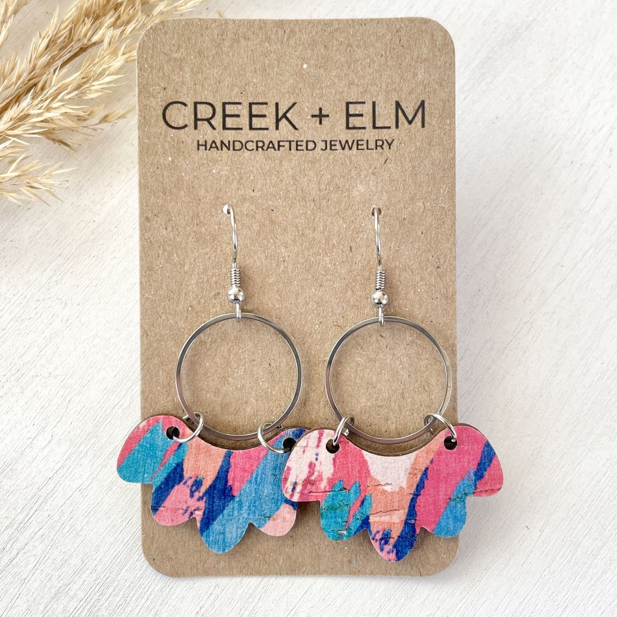 Colorful earrings on a Creek + Elm branded card with dried grass in the background